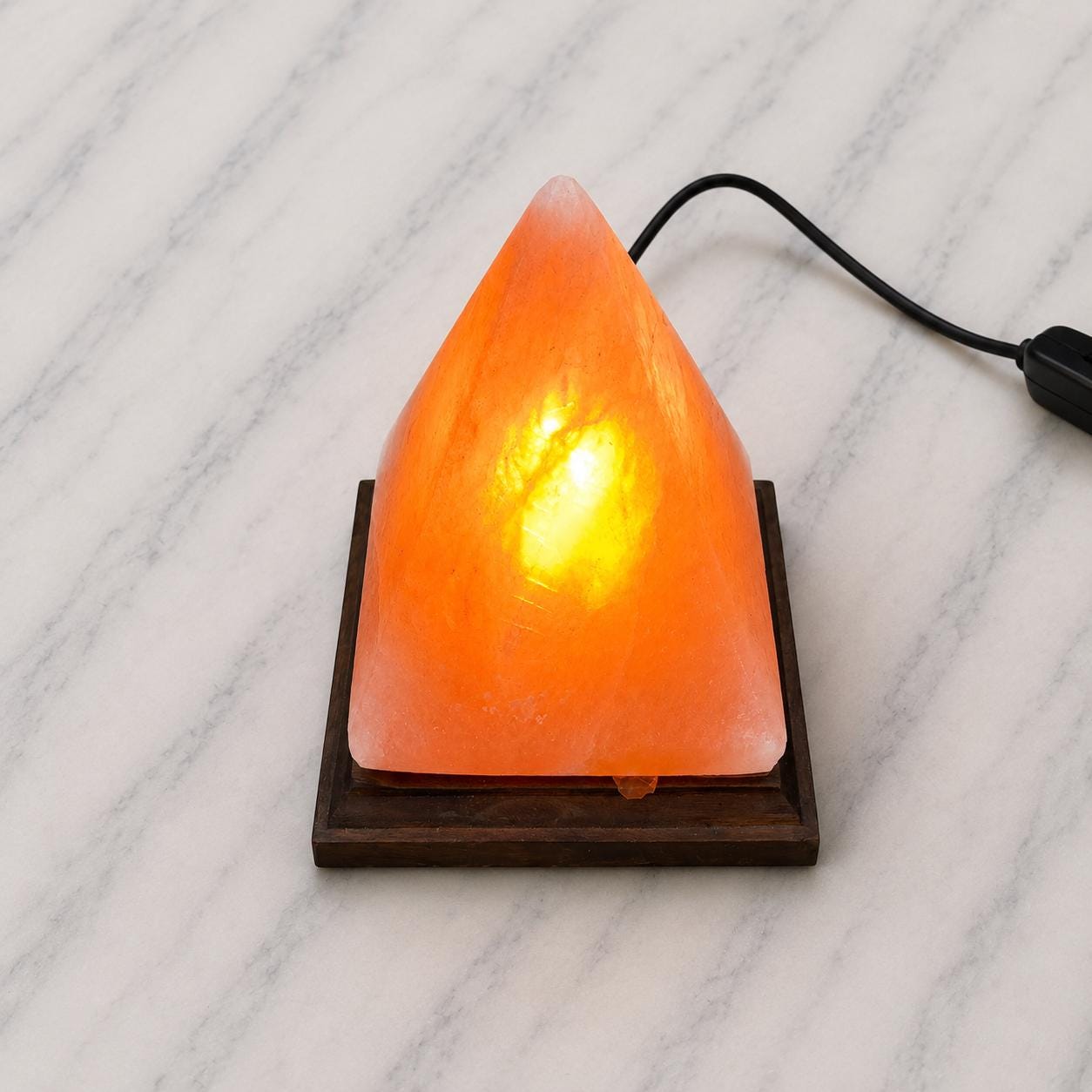 Pyramid Himalayan Salt Lamp glowing warm amber on a wood surface