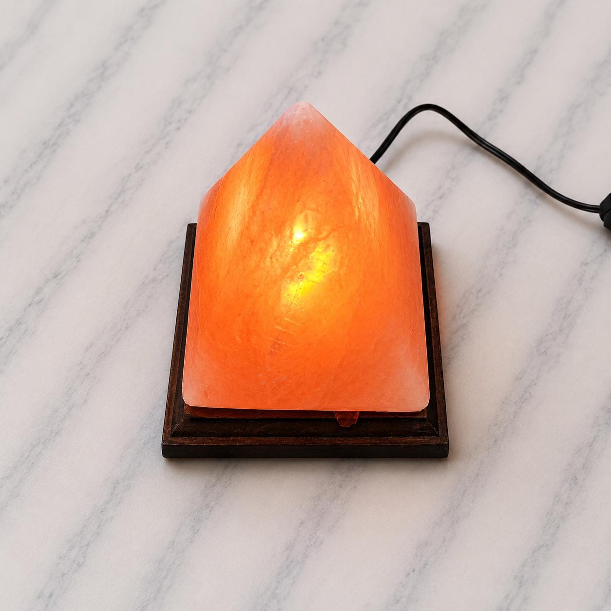 Pyramid Himalayan Salt Lamp glowing warm amber on a wood surface